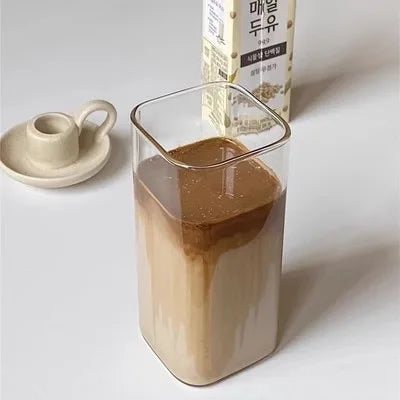 Glass of brown liquid next to a carton on a white surface