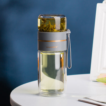 Clear glass water bottle with tea infuser on a white surface against a blue background