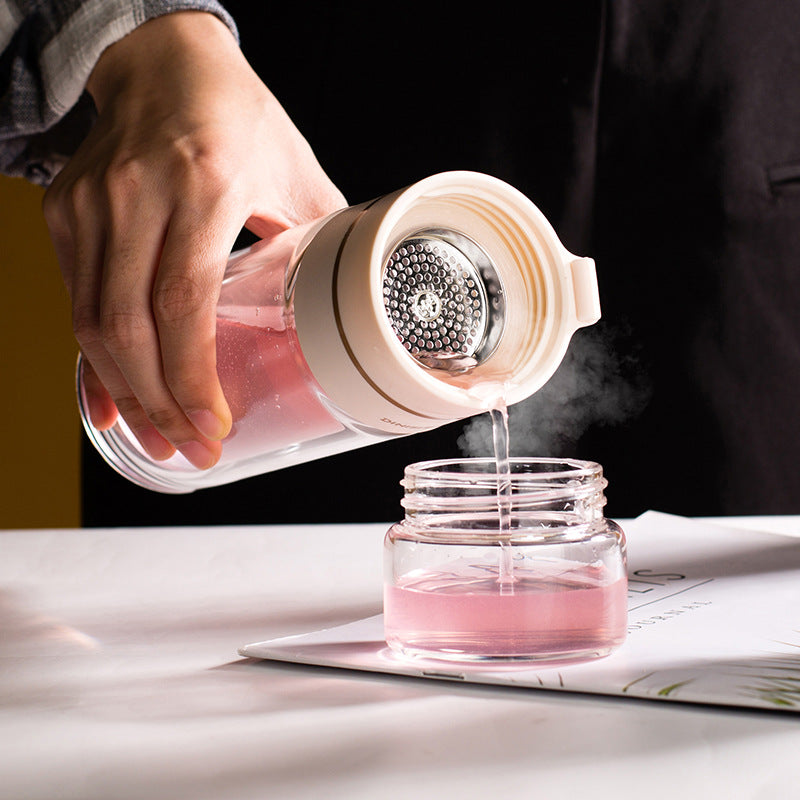 Hand pouring pink liquid from a container into a glass jar on a table.