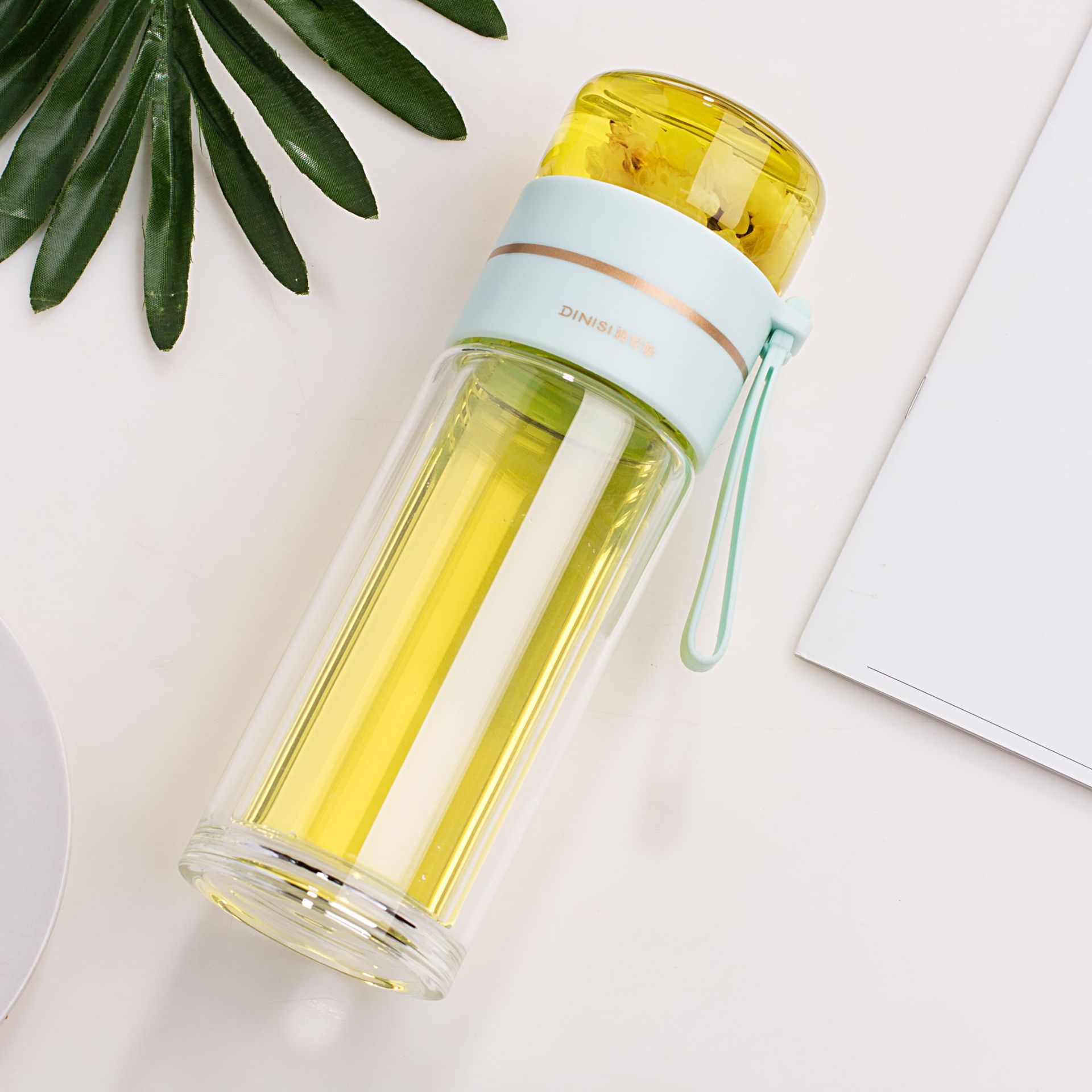 Clear glass water bottle with a yellow interior and light blue lid on a white surface.