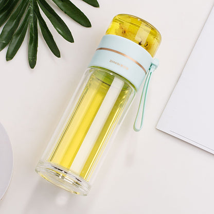 Clear glass water bottle with a yellow interior and light blue lid on a white surface.