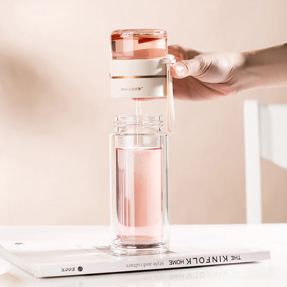 Hand holding a glass water bottle with a pink liquid on a white surface.