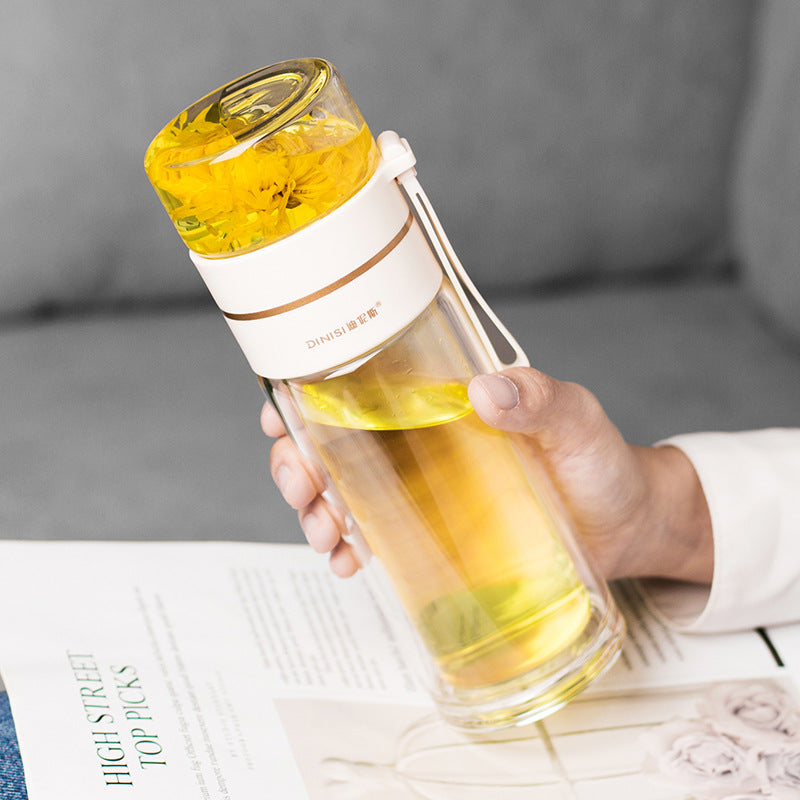 Hand holding a transparent water bottle with yellow liquid and a white lid, placed on a surface with a blurred background.
