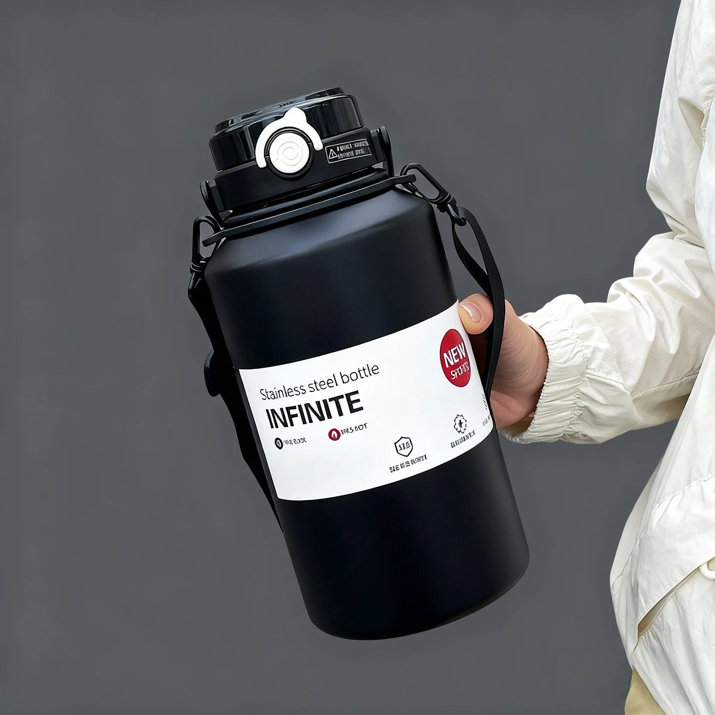 Person holding a black stainless steel bottle labeled 'INFINITE' against a gray background