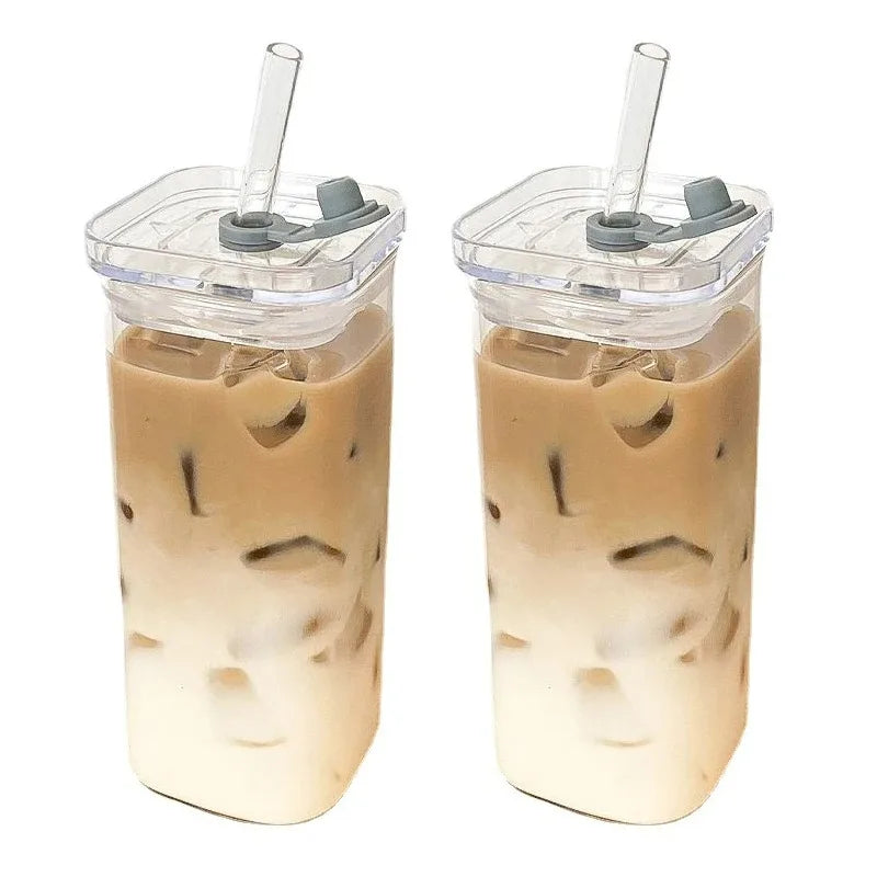 Two iced coffee drinks in clear tumblers with gray lids and straws on a white background.