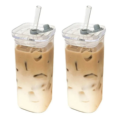 Two iced coffee drinks in clear tumblers with gray lids and straws on a white background.