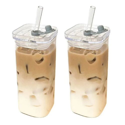 Two iced coffee drinks in clear tumblers with gray lids and straws on a white background.