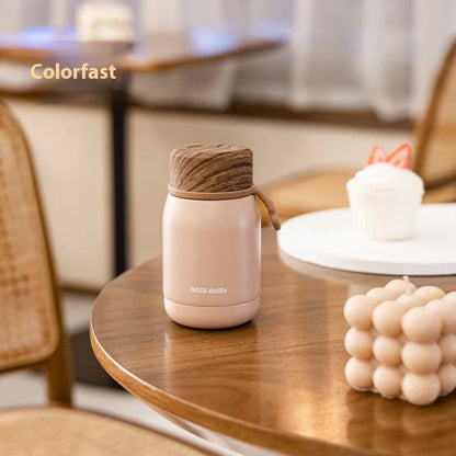 Pink thermos with wooden lid on a wooden table in a cozy indoor setting