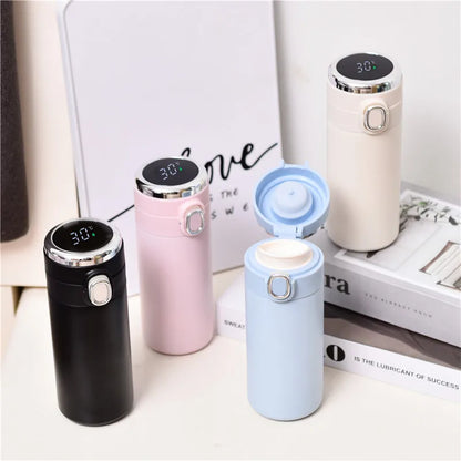 Four insulated travel mugs in different colors on a surface with a book in the background.