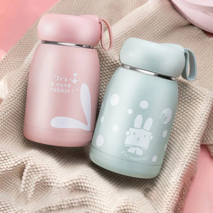 Two insulated cups, one pink and one light blue, with cartoon designs on a textured fabric background.