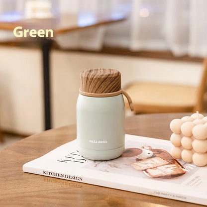 Light green thermos with wooden lid on a magazine on a wooden table