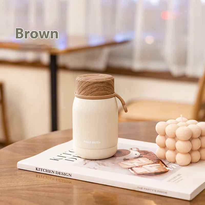 White thermos with brown lid on a magazine on a wooden table