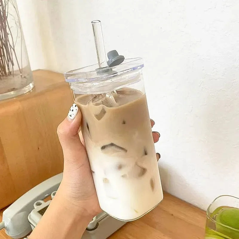 Hand holding a clear cup with iced coffee and a straw lid against a light background