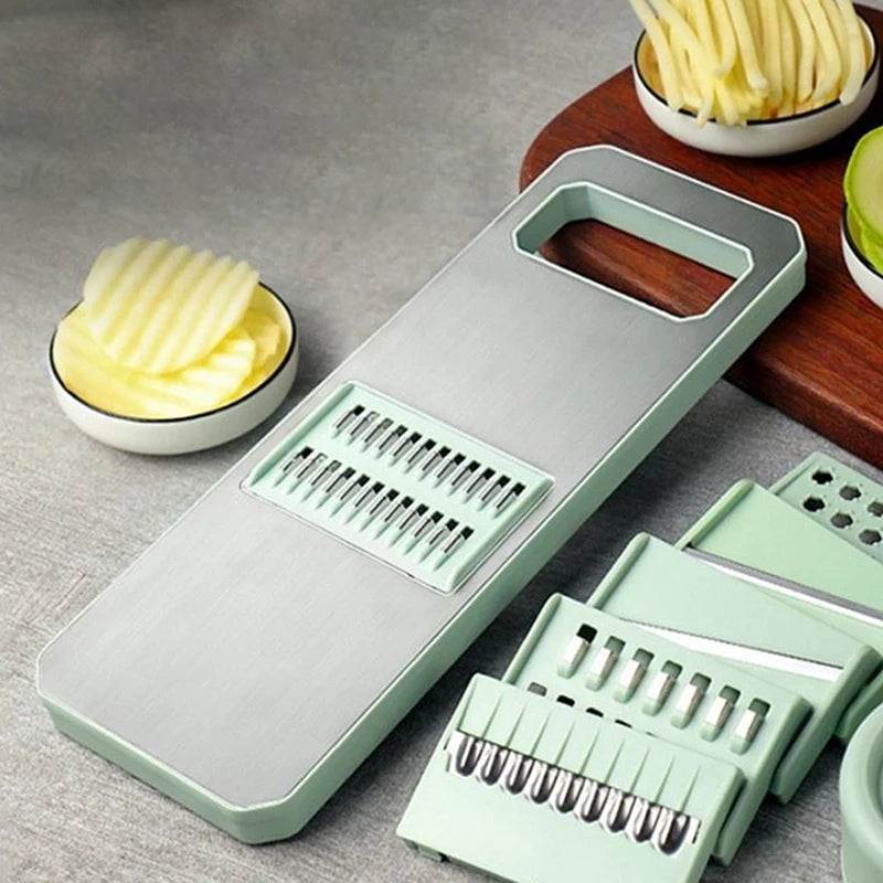 Green vegetable chopper with interchangeable blades on a gray surface with bowls of sliced vegetables.