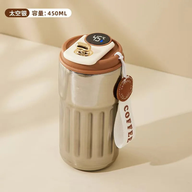 Stainless steel tumbler with brown lid and digital temperature display on a beige background