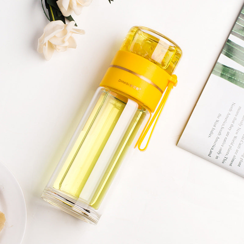 Yellow and clear glass water bottle on a white surface with flowers and a book in the background