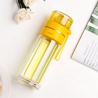Yellow and clear glass water bottle on a white surface with flowers and a book in the background
